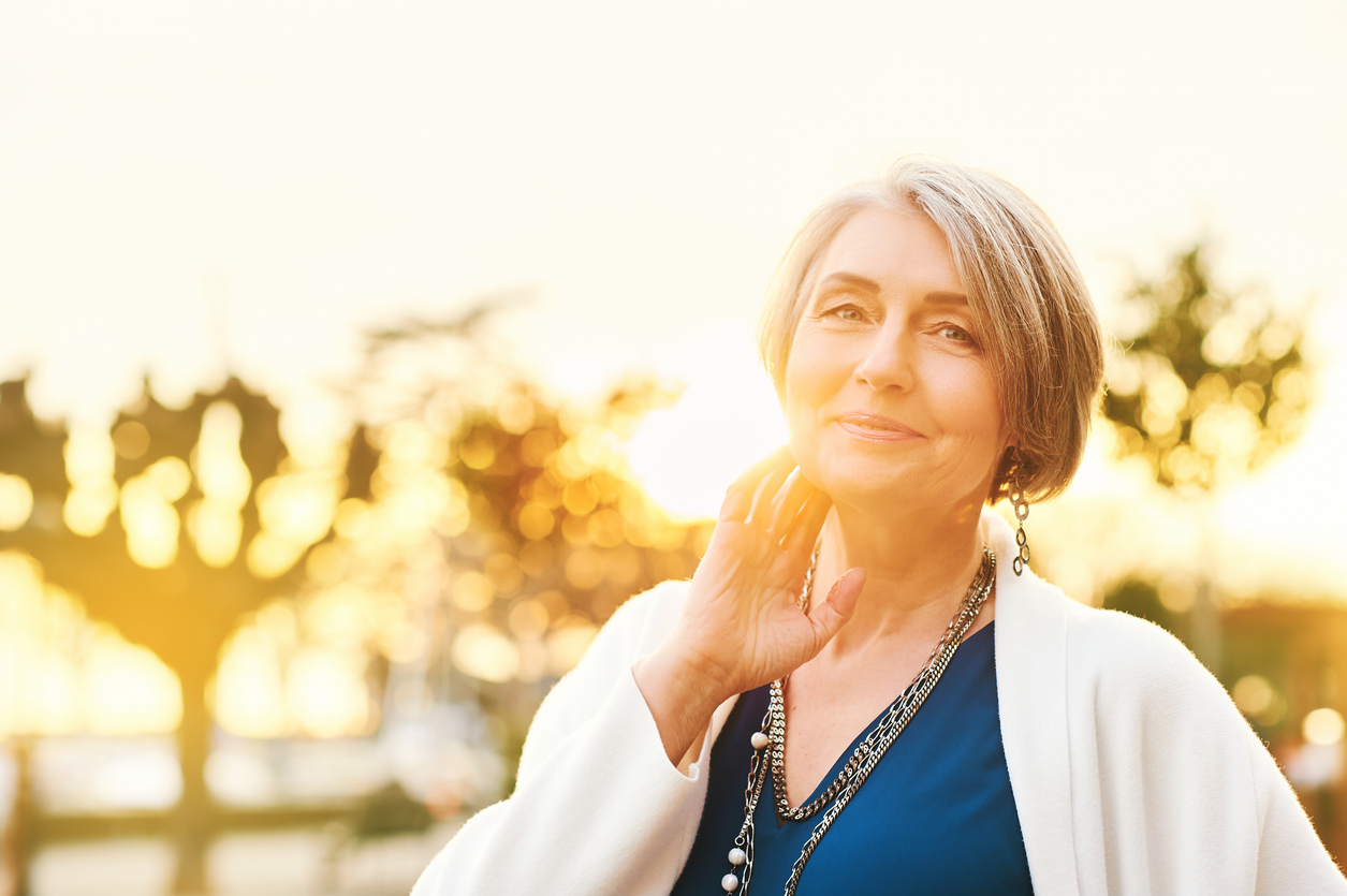 A confident older woman smiling outdoors at sunset, representing relief from chronic depression and insomnia after TMS therapy.